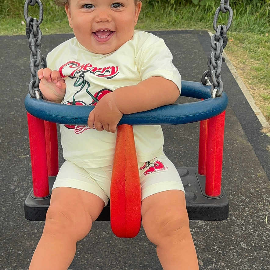 Kalilah is registered to the contest to win money with this photo: baby, bow, chain, child, cute, fun, greenery, happy, outdoor, play, playground, sandals, seat, shorts, smiling, socks, summer, swing, toddler, tshirt