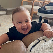 Adam is registered to the contest to win money with this photo: baby, smiling, happy, couch, blanket, living_room, child, furniture, indoor, person, armchair, carpet, wood_floor, door, cabinet, black_clothing, infant, playful, home, cozy