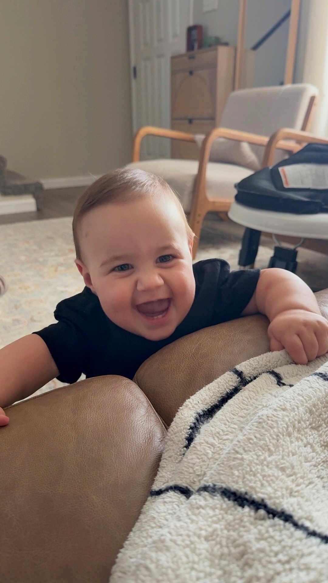 Adam is registered to the contest to win money with this photo: baby, smiling, happy, couch, blanket, living_room, child, furniture, indoor, person, armchair, carpet, wood_floor, door, cabinet, black_clothing, infant, playful, home, cozy