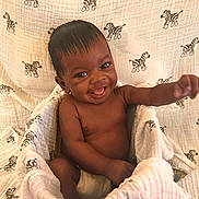 Tavante is registered to the contest to win money with this photo: baby, infant, smiling, happy, wrapped, blanket, zebra_pattern, diaper, cute, child, skin, face, hand, sitting, cozy, playful, indoors, portrait, young, expression
