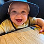 baby, child, smiling, blue_hat, yellow_shirt, table, happy, face, portrait, indoor, young_child, cute, person, closeup, headwear, infant, baby_hands, bright_eyes, cheerful, wooden_surface