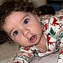 baby, child, curly_hair, blue_eyes, pajamas, reindeer_pattern, festive_clothing, lying_down, bed, close_up, face, hand, expression, indoor, person, cute, infant, portrait, sleepwear, holiday_theme