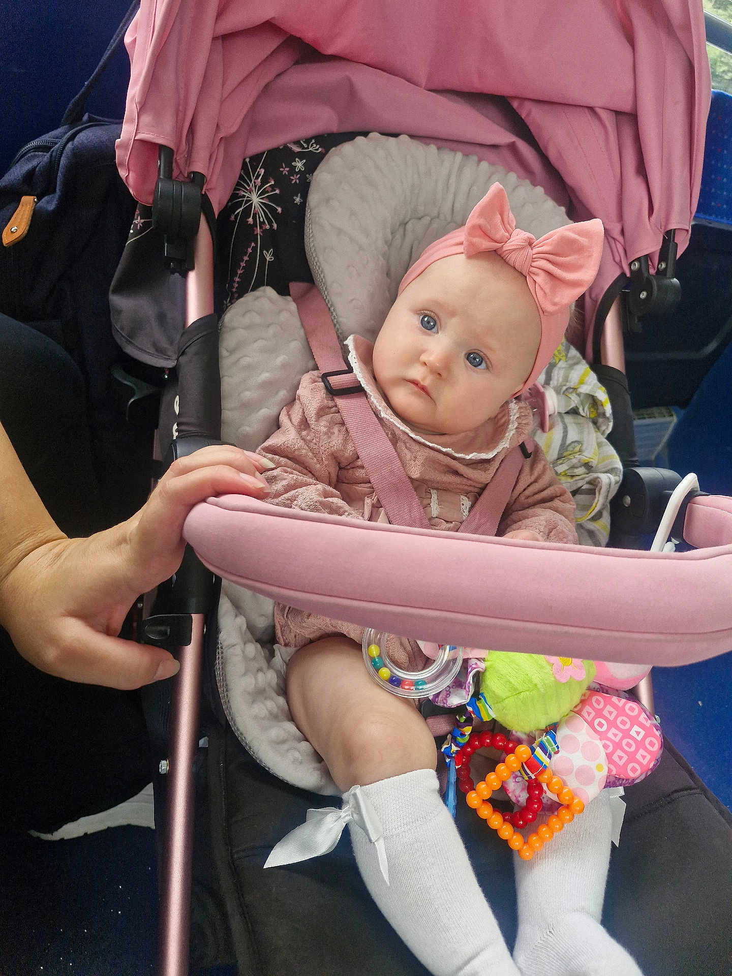 Lilah-Reign is registered to the contest to win money with this photo: baby, stroller, pink, headband, bow, toy, hand, socks, child, seatbelt, comfort, indoor, person, cute, infant, expression, clothing, sitting, blue_eyes, soft_toys