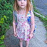 backpack, blue_eyes, child, daylight, dress, floral_dress, girl, greenery, mary_jane_shoes, outdoor, parked_car, plants, portrait, red_hair, road, serious_expression, shoes, sidewalk, standing, stone_wall