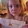 Bookie is registered to the contest to win money with this photo: blonde_hair, blue_eyes, child, close_up, document, dress, girl, holding_paper, home, household, indoors, kitchen, long_hair, photography, portrait, refrigerator, school_bus, seated, serious_expression, toddler