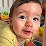 baby, infant, child, face, eyes, eyelashes, open_mouth, smile, cheeks, nose, hair, onesie, yellow_clothing, crib, toy, green_toy, blanket, close_up, portrait, indoor