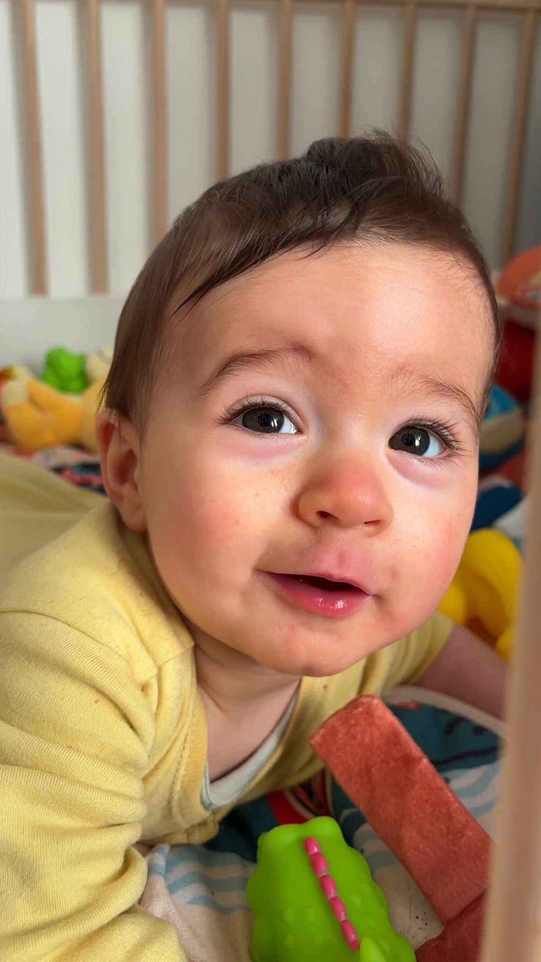 Tommy participe au concours pour gagner de l'argent avec cette photo : baby, infant, child, face, eyes, eyelashes, open_mouth, smile, cheeks, nose, hair, onesie, yellow_clothing, crib, toy, green_toy, blanket, close_up, portrait, indoor