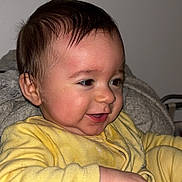 Tommy a rejoint le concours — aidez-le/la à gagner de superbes lots ! baby, infant, child, smile, yellow_clothing, onesie, blanket, gray_blanket, hand, cheeks, hair, face, close_up, indoor, portrait, flash, wall, cozy, sitting, happy
