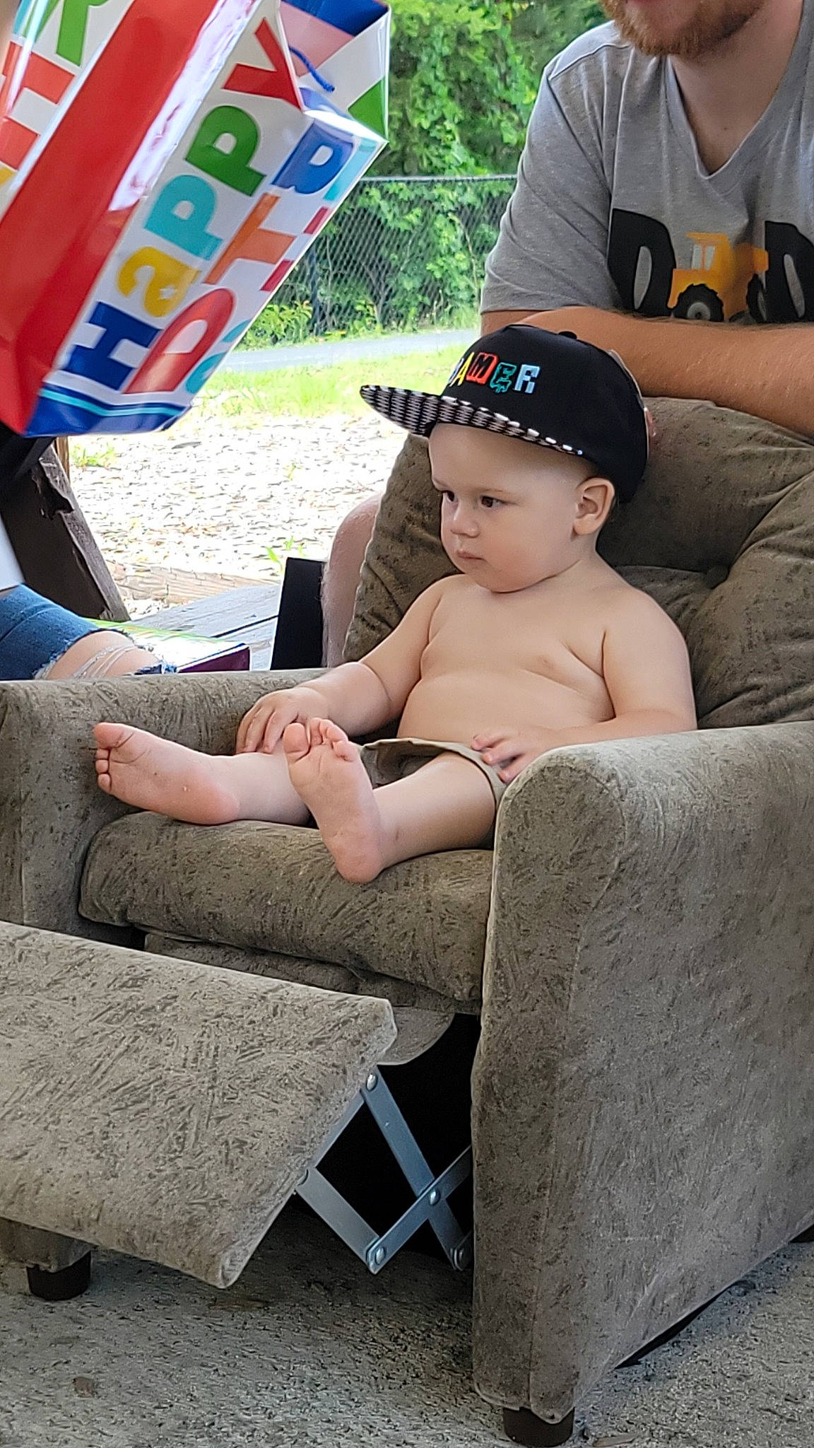 Emmett is registered to the contest to win money with this photo: baby, baby_toddler_clothing, baseball_cap, cap, comfort, event, eyewear, fedora, finger, grass, hat, headwear, lap, leisure, outdoor_furniture, person, recreation, shorts, sun_hat, t_shirt