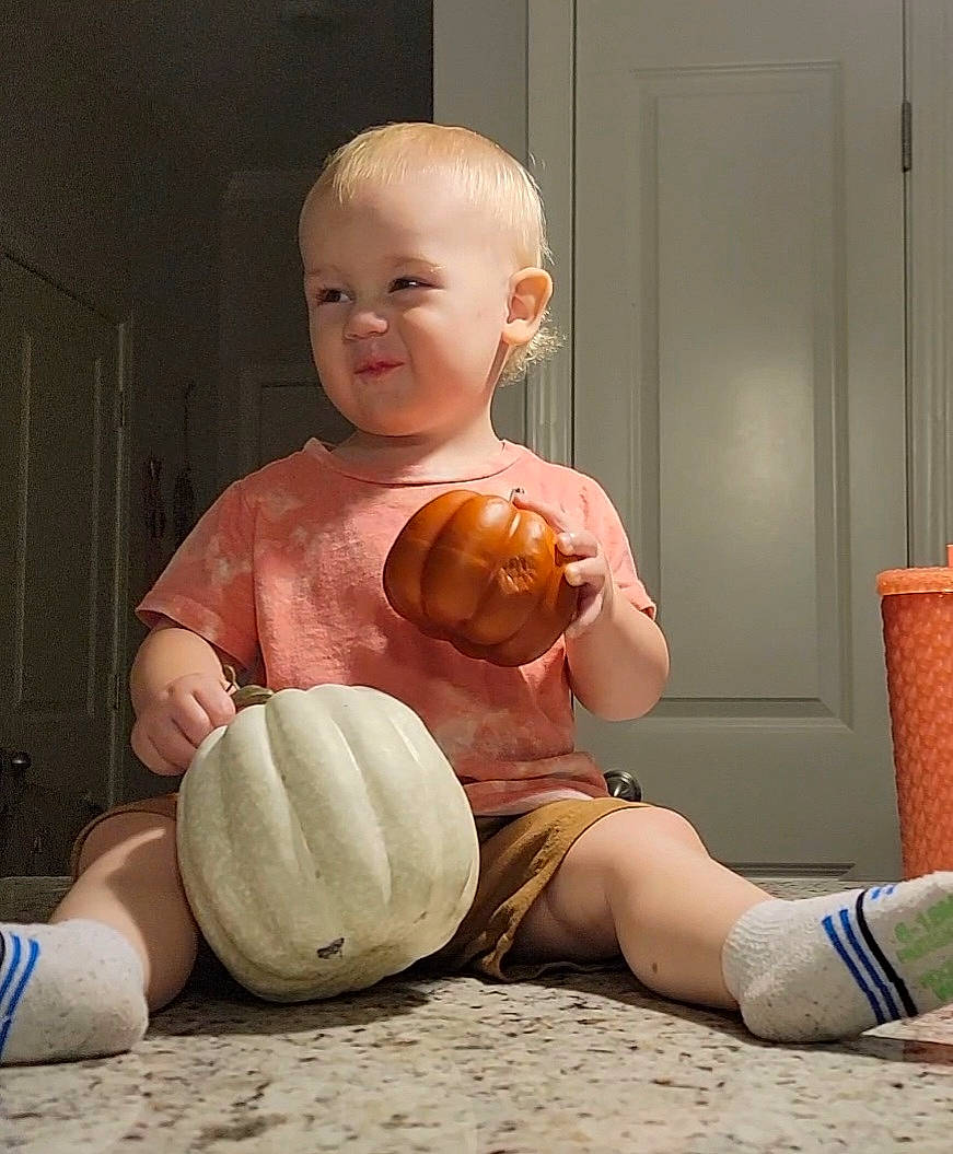 Emmett is registered to the contest to win money with this photo: ball, calabaza, chair, eye, finger, floor, flooring, gourd, hairstyle, joint, knee, muscle, orange, person, pumpkin, shoe, shoulder, thigh, vegetable, winter_squash