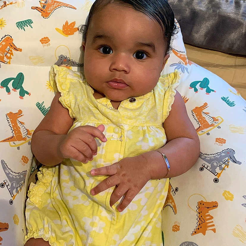 Naomi is registered to the contest to win money with this photo: accessories, baby, bed, bedroom, bodypart, clothing, couch, cushion, dress, face, finger, furniture, hand, head, homedecor, indoors, person, photography, portrait, sitting