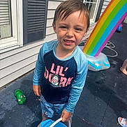 Jackson is registered to the contest to win money with this photo: child, boy, bucket, water, swimwear, rainbow, inflatable, outdoor, patio, wet_floor, window, house_siding, summer, play, barefoot, expression, fun, plastic_shoe, sunlight, daytime