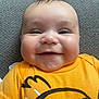 baby, smiling, yellow_shirt, cartoon_print, chubby_cheeks, face, infant, cute, happy, portrait, closeup, lying_down, textile_background, short_hair, indoors, child, toddler, skin, expression, person