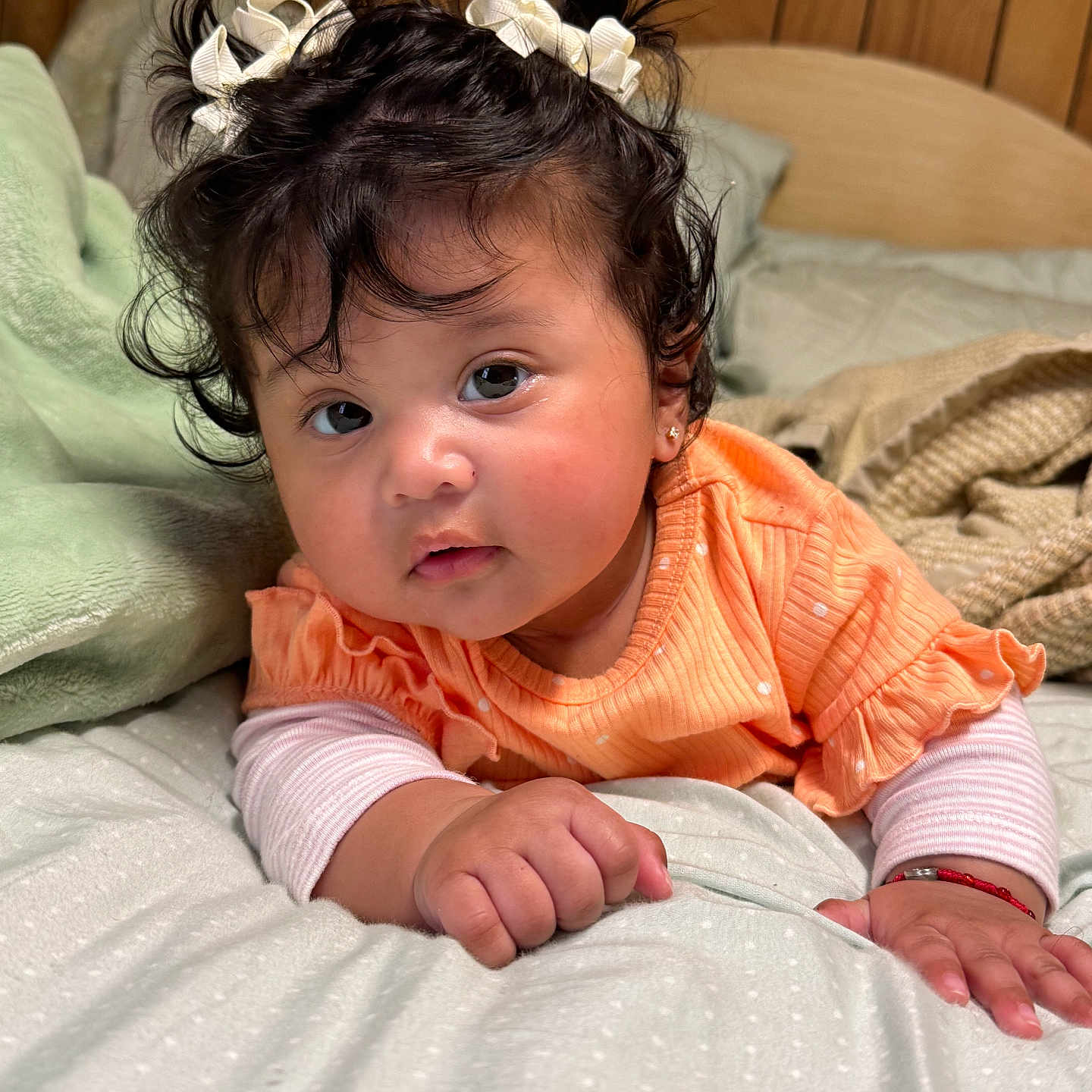 Aitana joined the competition — help win amazing prizes! baby, bed, blanket, bows, child, closeup, cozy, curly_hair, cute, expression, face, hands, indoor, infant, orange_clothing, person, portrait, sleeping_area, soft_lighting, wood_paneling