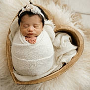 Aitana is registered to the contest to win money with this photo: newborn, baby, swaddled, sleeping, headband, white_wrap, heart_shaped_bowl, fur, soft_texture, cozy, peaceful, infant, portrait, closeup, indoors, cute, hands, resting, blanket, adorable