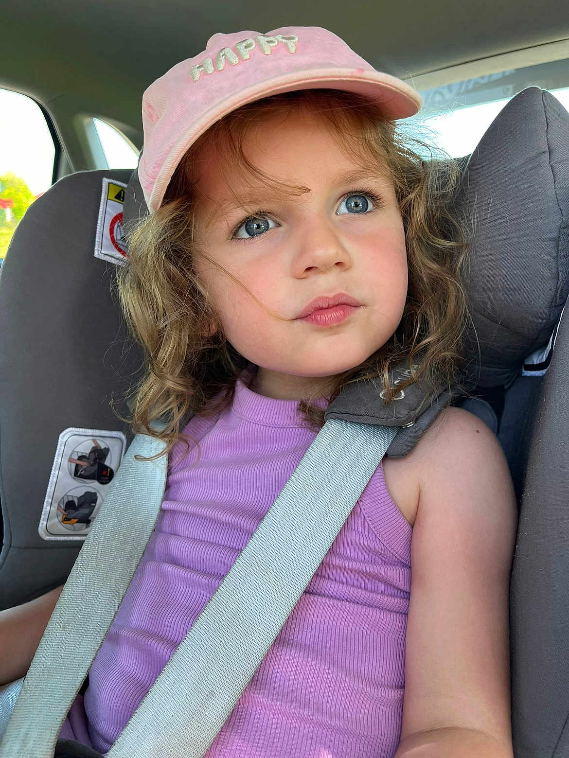 Clémence participe au concours pour gagner de l'argent avec cette photo : child, girl, car_seat, seatbelt, pink_cap, purple_tank_top, curly_hair, blue_eyes, car_interior, safety_strap, window, daylight, portrait, cute, young_person, expression, casual_clothing, closeup, seat, summer
