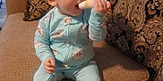 Abraylee joined the competition — help win amazing prizes! baby, child, onesie, blue_clothing, couch, living_room, tube, chewing, patterned_cushion, blanket, furniture, curious, sitting, indoors, infant, person, footwear, head, face, hand