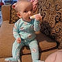 baby, child, onesie, blue_clothing, couch, living_room, tube, chewing, patterned_cushion, blanket, furniture, curious, sitting, indoors, infant, person, footwear, head, face, hand