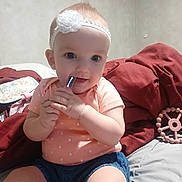 Abraylee is registered to the contest to win money with this photo: baby, infant, headband, flower, polka_dot, shirt, shorts, bed, blanket, toy, chewing, cute, child, indoors, person, playful, skin, hand, face, sitting