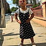 child, girl, sunglasses, dress, white_shirt, sandals, sidewalk, shadow, sunny, outdoor, urban, building, street, confident, pose, fashion, accessories, summer, person, standing