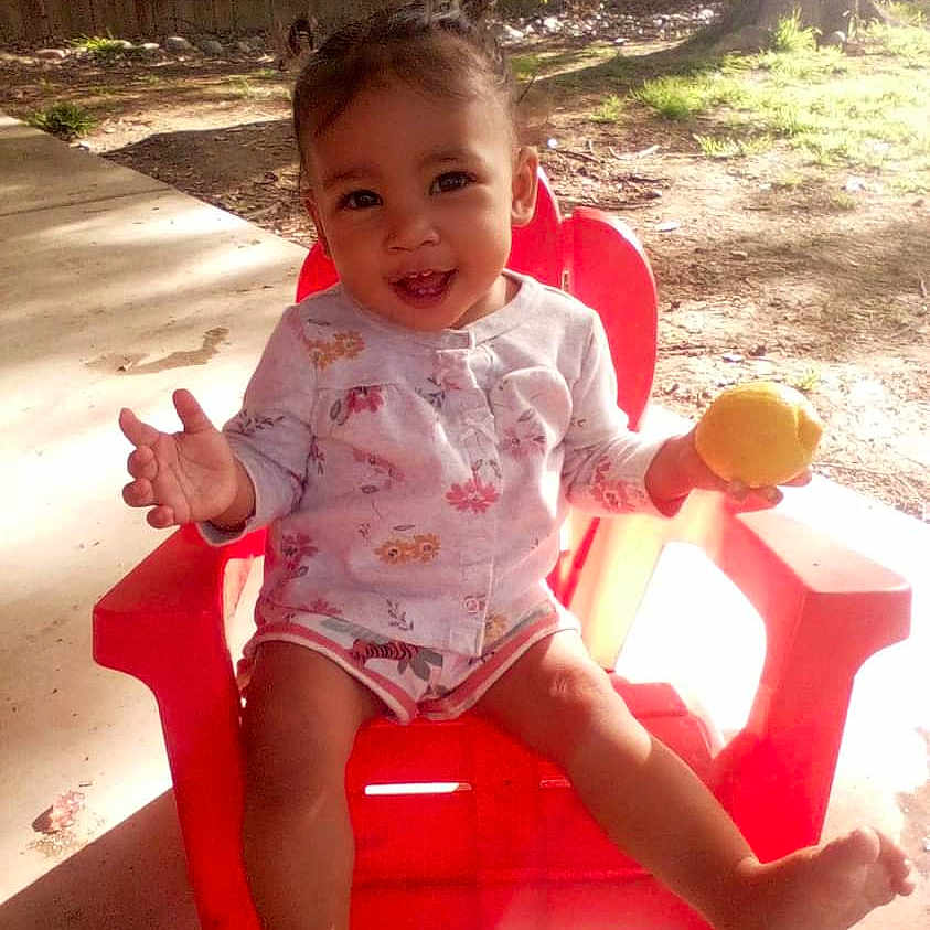 Amya is registered to the contest to win money with this photo: baby, backyard, chair, clothing, face, food, fruit, furniture, grass, head, nature, outdoors, person, photography, plant, portrait, shorts, sitting, summer, yard