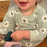 toddler, child, smiling, sitting, stairs, hair_clip, green_shirt, daisy_pattern, mustard_pants, holding_phone, happy, indoor, wooden_stairs, cute, young_child, portrait, casual_clothing, small_earrings, playful, light_hair