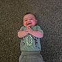 Emerson is registered to the contest to win money with this photo: baby, infant, smile, happy, carpet, gray_carpet, lying_down, hands, face, head, onesie, shirt, pants, sweatpants, printed_number, checker_pattern, green_shirt, texture, indoor, portrait