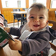 Arthur a rejoint le concours — aidez-le/la à gagner de superbes lots ! baby, child, smiling, happy, high_chair, jacket, bib, table, chair, indoor, menu, wooden_table, window, daylight, person, face, cute, infant, holding, restaurant