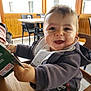 baby, child, smiling, happy, high_chair, jacket, bib, table, chair, indoor, menu, wooden_table, window, daylight, person, face, cute, infant, holding, restaurant