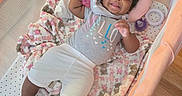 Akira is registered to the contest to win money with this photo: baby, child, smiling, playpen, blanket, toy, sandals, bow, curly_hair, pink, clothing, happy, floor, footwear, infant, person, indoors, cute, resting, toddler