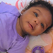 Akira is registered to the contest to win money with this photo: baby, infant, child, purple_shirt, pacifier, curly_hair, smile, close_up, lying_down, soft_surface, cute, face, eyes, mouth, skin, head, baby_clothes, indoors, happy, portrait