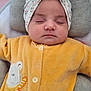 baby, sleeping, headwrap, yellow_onesie, bear_design, cushion, soft_toys, infant, cute, peaceful, child, portrait, indoors, resting, face, clothing, headwear, closeup, cozy, adorable