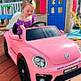 child, toddler, toy_car, pink_car, outdoor, playground, playhouse, smiling, happy, summer, daylight, backyard, slide, vehicle, person, short_hair, purple_clothing, wooden_floor, sunlight, cute