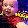 Ryan is registered to the contest to win money with this photo: baby, child, person, face, smiling, indoor, colorful, red_shirt, closeup, adult, blue_ceiling, yellow_wall, lights, happy, portrait, people, hand, casual_clothing, expression, background