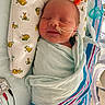 Carl is registered to the contest to win money with this photo: newborn, baby, infant, hospital, medical_tube, swaddled, blanket, pillow, sleeping, smile, face, person, bed, healthcare, cute, child, striped_blanket, nursery, resting, soft_fabric