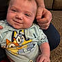 baby, child, infant, smiling, hand, tshirt, cartoon, indoor, carpet, couch, person, diaper, clip, holding, face, cute, closeup, seated, human, portrait