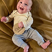 Ollie joined the competition — help win amazing prizes! baby, smiling, infant, milestone, wooden_sign, striped_clothing, gray_pants, blanket, happy, lying_down, cute, small_hands, small_feet, face, human, child, indoors, portrait, cozy, milestone_marker