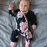 Maëve participe au concours pour gagner de l'argent avec cette photo : baby, infant, child, onesie, floral_pattern, bed, striped_bedding, foot, hand, face, sleepwear, pink, black, green, white, cute, lying_down, portrait, indoors, calm