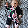 baby, infant, child, onesie, floral_pattern, bed, striped_bedding, foot, hand, face, sleepwear, pink, black, green, white, cute, lying_down, portrait, indoors, calm