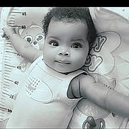 Kea'Ari is registered to the contest to win money with this photo: baby, infant, child, face, eyes, arms, curly_hair, smile, onesie, baby_mat, cartoon, measurement_scale, pacifier, cute, portrait, laying_down, indoors, soft_lighting, black_and_white, close_up