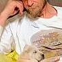 man, cap, beard, couch, puppy, dog, sleeping, white_shirt, blue_jeans, indoor, relaxing, resting, pet, companion, casual, seated, human, animal, cute, cozy