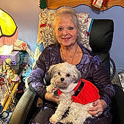 Ellie Rose is registered to the contest to win money with this photo: chair, cozy, decoration, dog, furniture, gray_hair, happy, home, indoor, jewelry, lamp, long_sleeves, pet, portrait, quilt, red_dress, seated, small_dog, smiling, woman