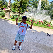 Ethan a rejoint le concours — aidez-le/la à gagner de superbes lots ! child, boy, smiling, outdoor, park, fountain, flowers, greenery, sunlight, cap, tshirt, shorts, sneakers, pigeon, pathway, trees, nature, daytime, backpack, gesture