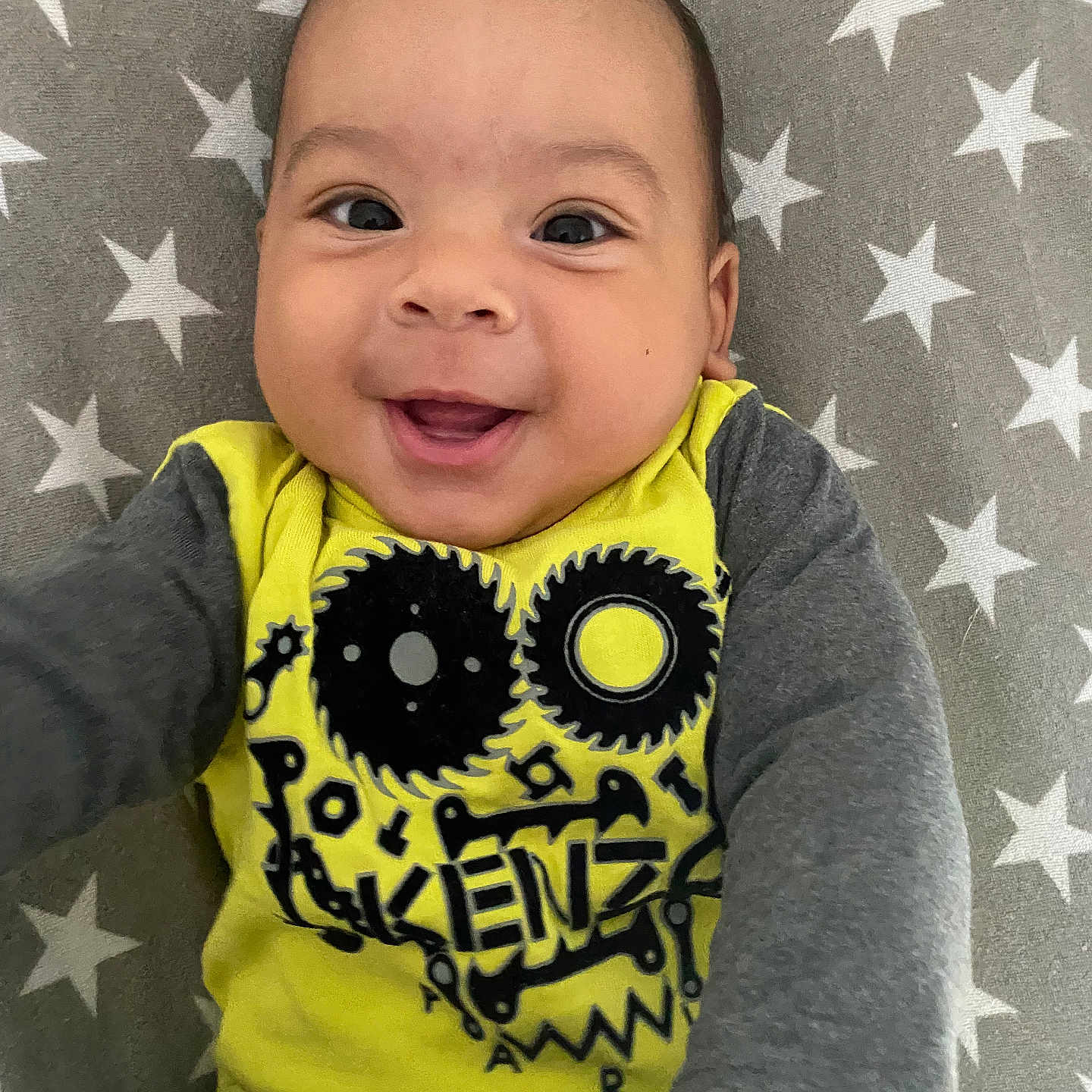 Hayven a rejoint le concours — aidez-le/la à gagner de superbes lots ! baby, cheerful, child, closeup, clothing, cute, face, gray_sleeves, hand, happy, indoor, infant, lying_down, patterned_blanket, person, portrait, smiling, stars, yellow_shirt, young_child
