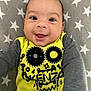baby, smiling, face, yellow_shirt, grey_sleeves, star_pattern, blanket, child, happy, infant, portrait, cute, person, clothing, sitting, indoors, young_child, head, eyes, mouth