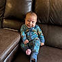 baby, child, pajamas, blue_clothing, smile, face, sitting, couch, leather, indoors, young_child, foot, hand, comfort, portrait, cute, happy, cozy, infant, relaxation