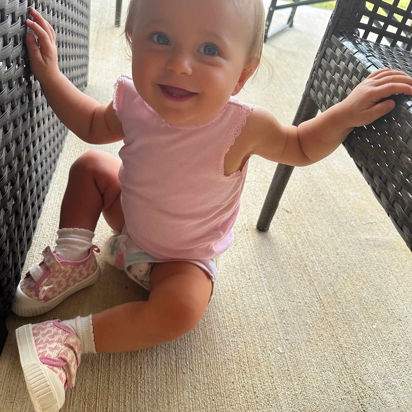 Hailey Grace is registered to the contest to win money with this photo: baby, blue_eyes, casual_clothing, child, concrete_floor, cute, furniture, happy, outdoor, person, pink_shoes, pink_top, playful, pony_tail, sitting, smiling, sunlight, toddler, wicker_chair, young_child