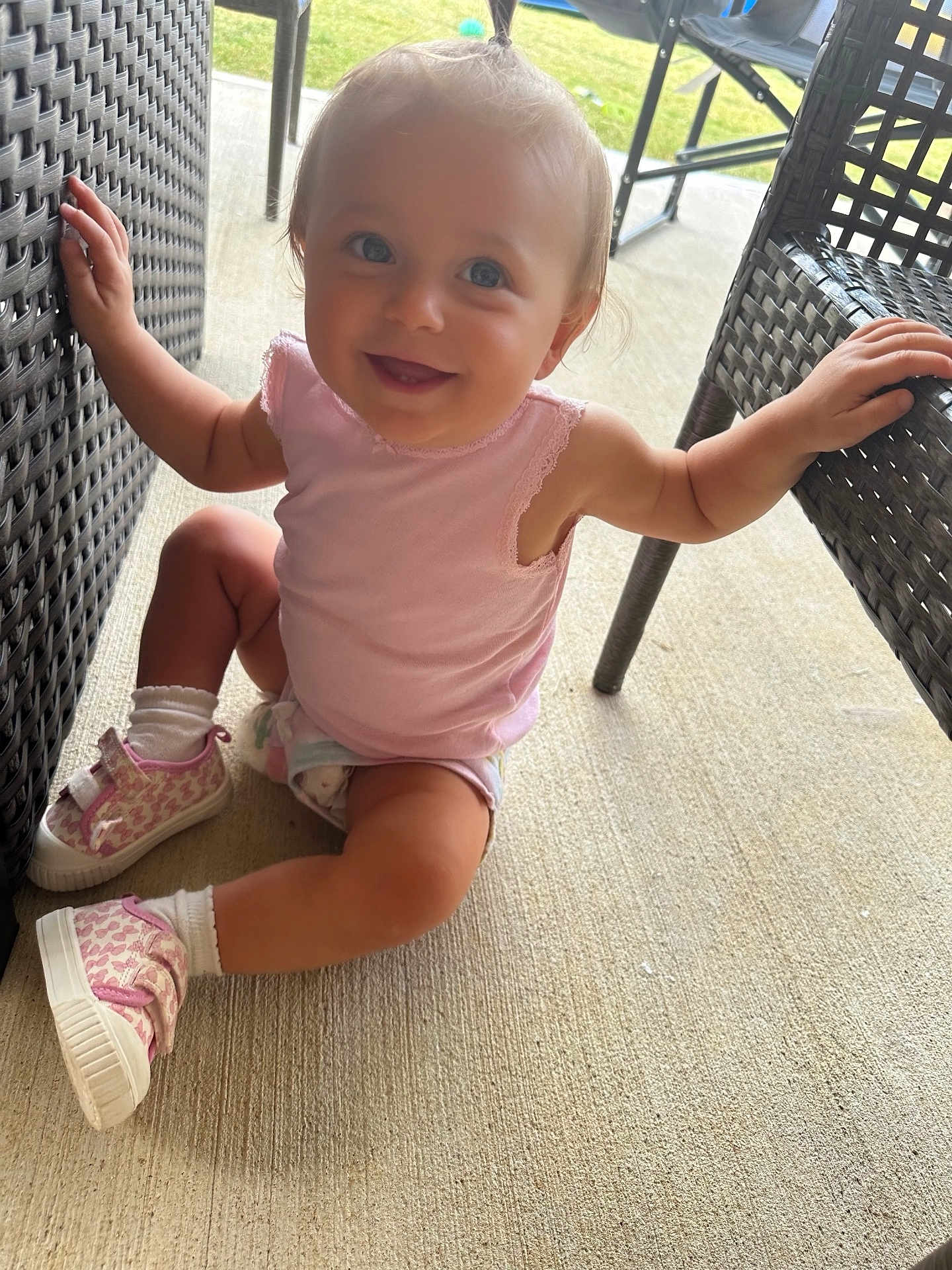 Hailey Grace is registered to the contest to win money with this photo: toddler, child, smiling, sitting, pink_shoes, pink_top, pony_tail, wicker_chair, outdoor, concrete_floor, happy, young_child, cute, blue_eyes, casual_clothing, playful, sunlight, furniture, baby, person