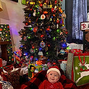 Angel L. B. joined the competition — help win amazing prizes! baby, christmas_tree, christmas_lights, presents, gift_bags, santa_hat, red_clothing, blanket, holiday, decorations, indoor, festive, smiling, child, holiday_season, ornaments, toys, home, curtains, photography