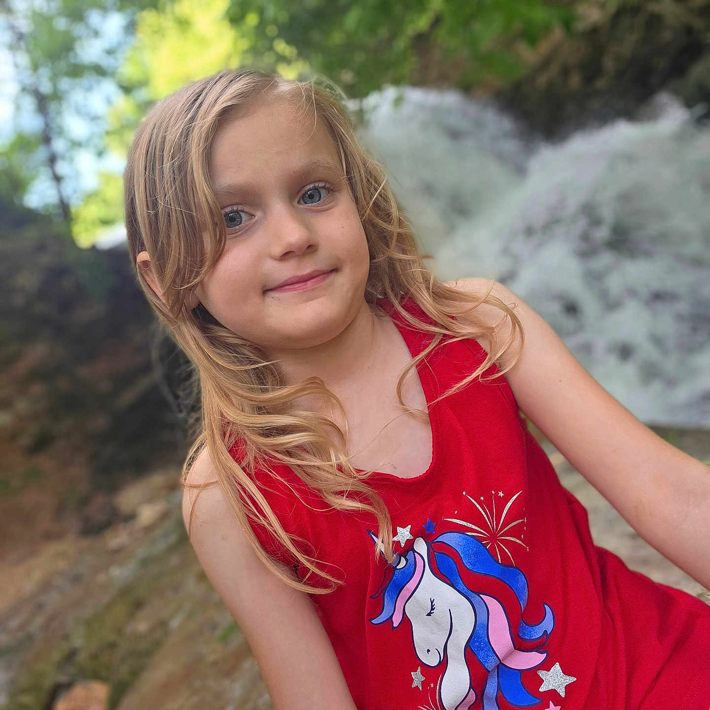 Airabella joined the competition — help win amazing prizes! child, girl, blonde_hair, red_tank_top, unicorn_graphic, outdoor, waterfall, nature, greenery, smiling, portrait, summer, casual_clothing, happy, young, scenic, background_blur, daylight, cute, posing